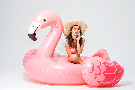 穿粉色比基尼的可爱卖女坐在火烈鸟游泳圈图片