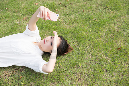 青春学生躺草地用手机自拍图片