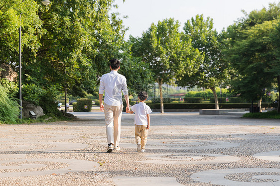 公园里牵手散步父子背影