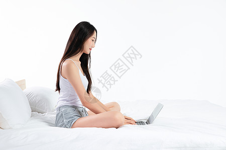 年轻女性坐在床上玩电脑背景图片