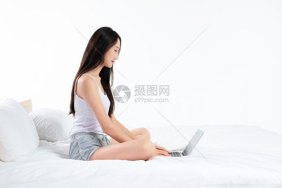 年轻女性坐在床上玩电脑图片