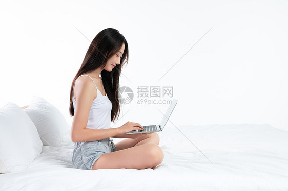 年轻女性坐在床上玩电脑图片