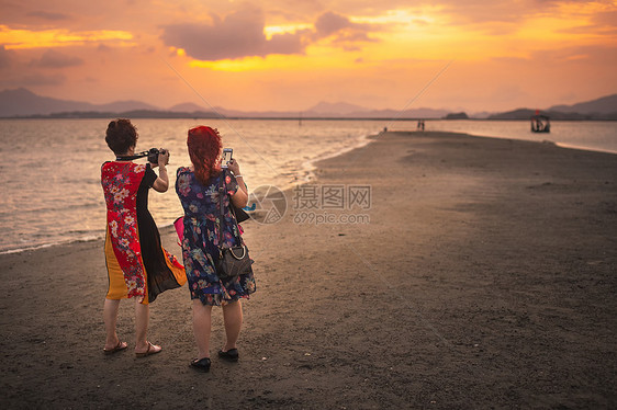 广东惠东盐洲岛海岸夕阳晚霞下拍照的游人图片