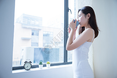 年轻女性窗边喝水图片