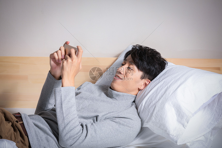 躺在枕头上玩手机的男人图片
