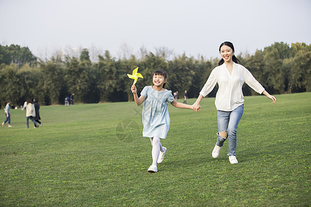 女儿和妈妈拿着风车在草坪上奔跑背景图片