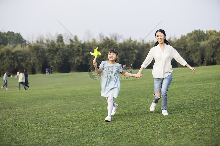 女儿和妈妈拿着风车在草坪上奔跑图片