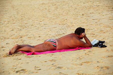 俯卧在沙滩上看书的男人图片