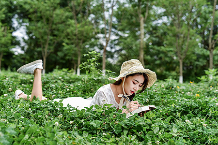 花园看书带着帽子躺着写字的女生背景