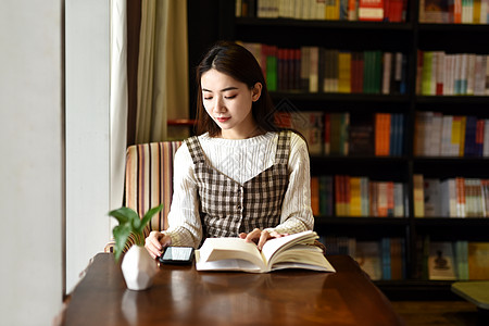 女生玩手机书店坐着阅读的女学生背景