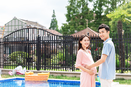 孕妇和丈夫面对面站在泳池旁背景图片