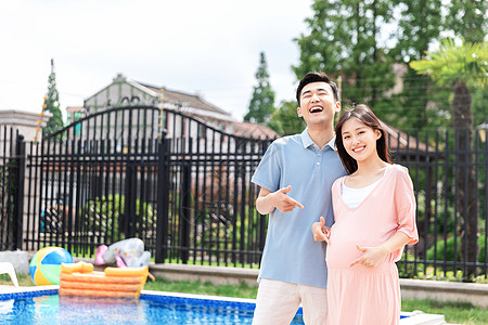 一起去游泳丈夫和孕妇一起站在户外泳池旁背景