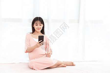 一个孕妇在客厅纱窗旁边使用手机背景图片