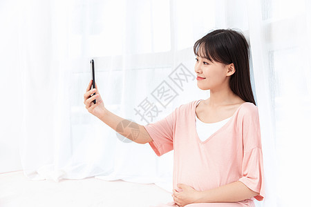 孕妇在客厅纱窗旁边使用手机自拍图片