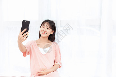 孕妇在客厅纱窗旁边使用手机自拍图片