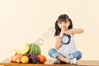 小女孩坐在水果旁玩闹钟图片