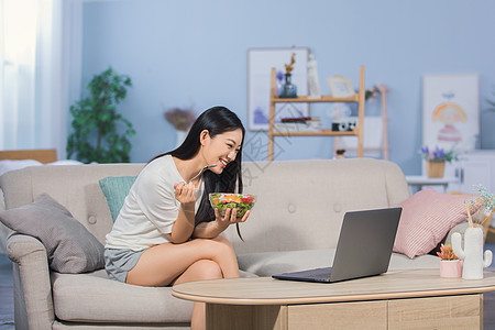 女性坐在沙发上吃东西看电脑高清图片素材