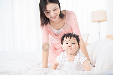 抱着花小女孩妈妈在床上逗宝宝玩背景