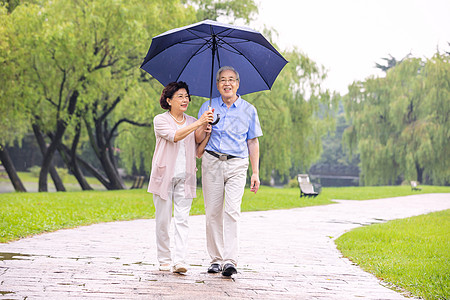 老年旅游老年夫妇在公园雨中散步背景