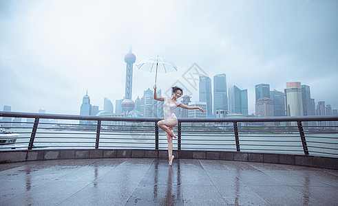 雨中舞蹈在城市建筑下撑伞的跳芭蕾舞者背景