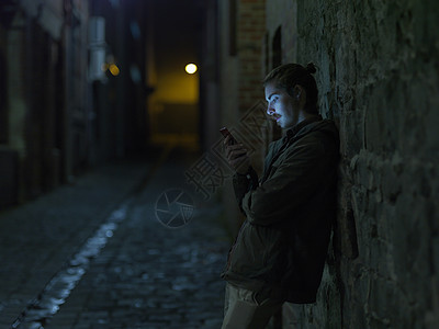 年轻人在街上晚上靠在墙上用智能手机图片
