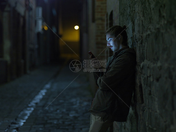 年轻人在街上晚上靠在墙上用智能手机图片