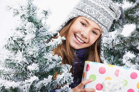 拿着礼物的女孩，在白雪皑皑的树旁背景图片