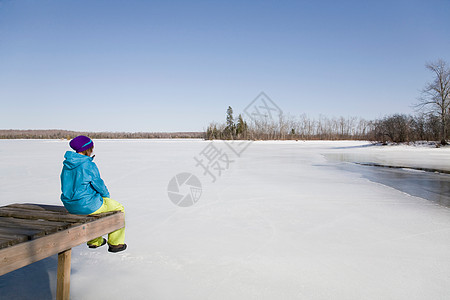 在结冰的湖边码头上坐着的女性高清图片