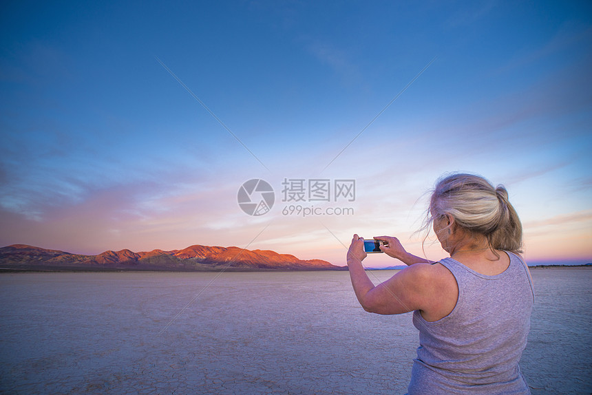 一位女士在智能手机上拍摄盐滩和远处山脉的照片图片