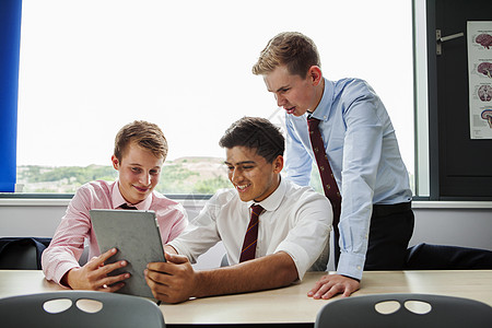 十几岁的男生坐在桌旁用数码平板电脑图片