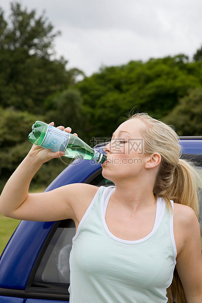 年轻女子在电动车旁喝水图片