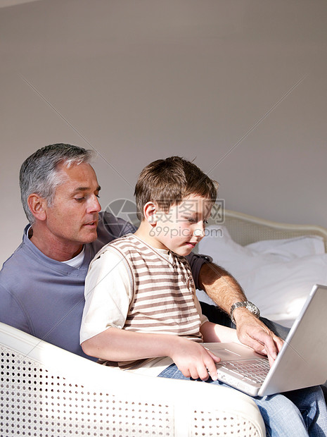 父亲和儿子在卧室使用笔记本电脑图片