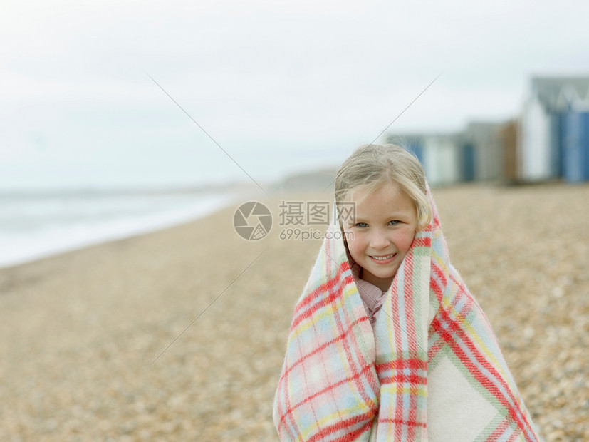 小女孩在海滩上蜷缩在毯子里图片