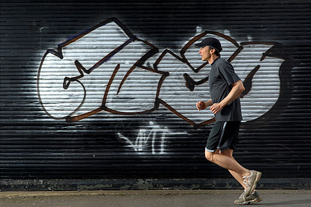 在街上路过涂鸦的男跑步者图片