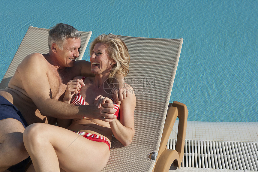 老夫妇在泳池边的日光浴床上欢笑图片