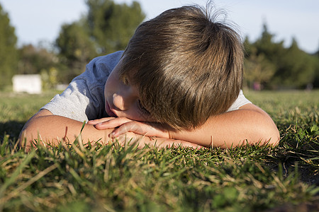 一个闷闷不乐的男孩，低着头躺在公园的草地上图片