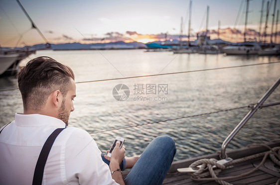 意大利撒丁岛卡利亚里游艇上使用智能手机的年轻人图片