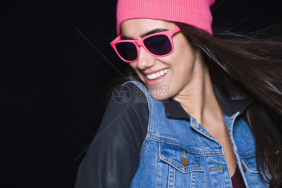年轻女子的肖像，戴着粉色帽子和太阳镜，微笑着图片