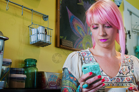 在厨房里用智能手机阅读短信的粉红色头发的年轻女子图片