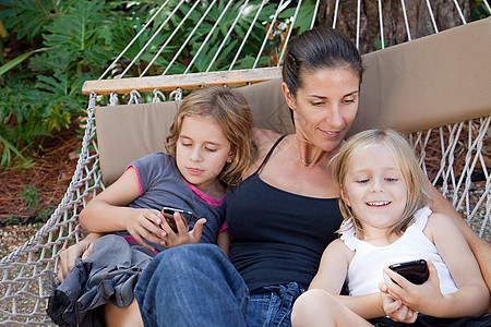 带智能手机的吊床上的母亲和女儿图片