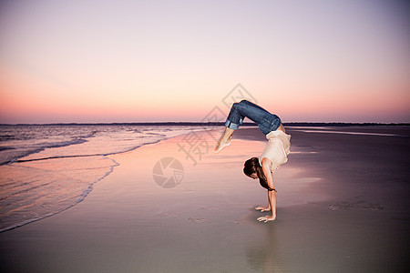 日落时分在海滩上做倒立的女人图片