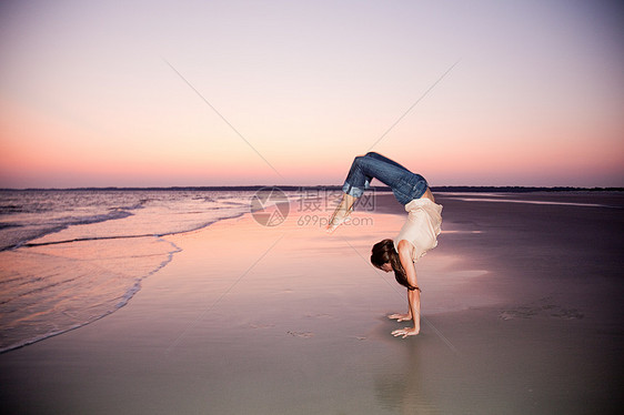 日落时分在海滩上做倒立的女人图片