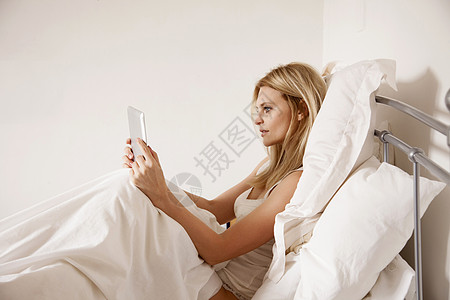 中年妇女坐在床上使用平板电脑图片