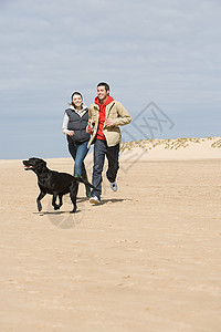 一对夫妇带着狗在海滩上奔跑图片