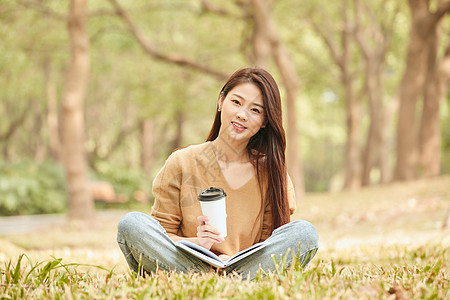 年轻女性草地上看书喝咖啡高清图片