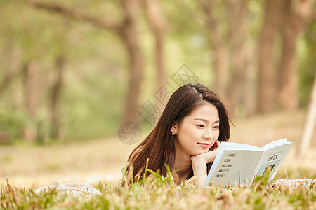 年轻女性趴在草地上看书图片