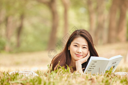 年轻女性趴在草地上看书图片