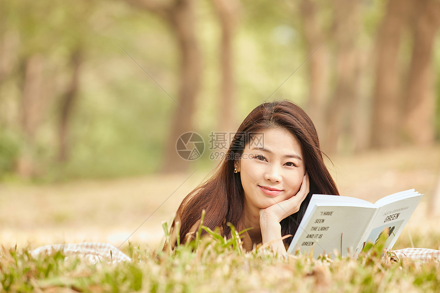 年轻女性趴在草地上看书图片