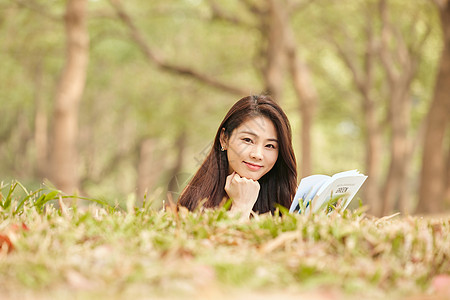 年轻女性趴在草地上看书背景