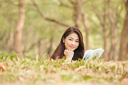 年轻女性趴在草地上看书图片